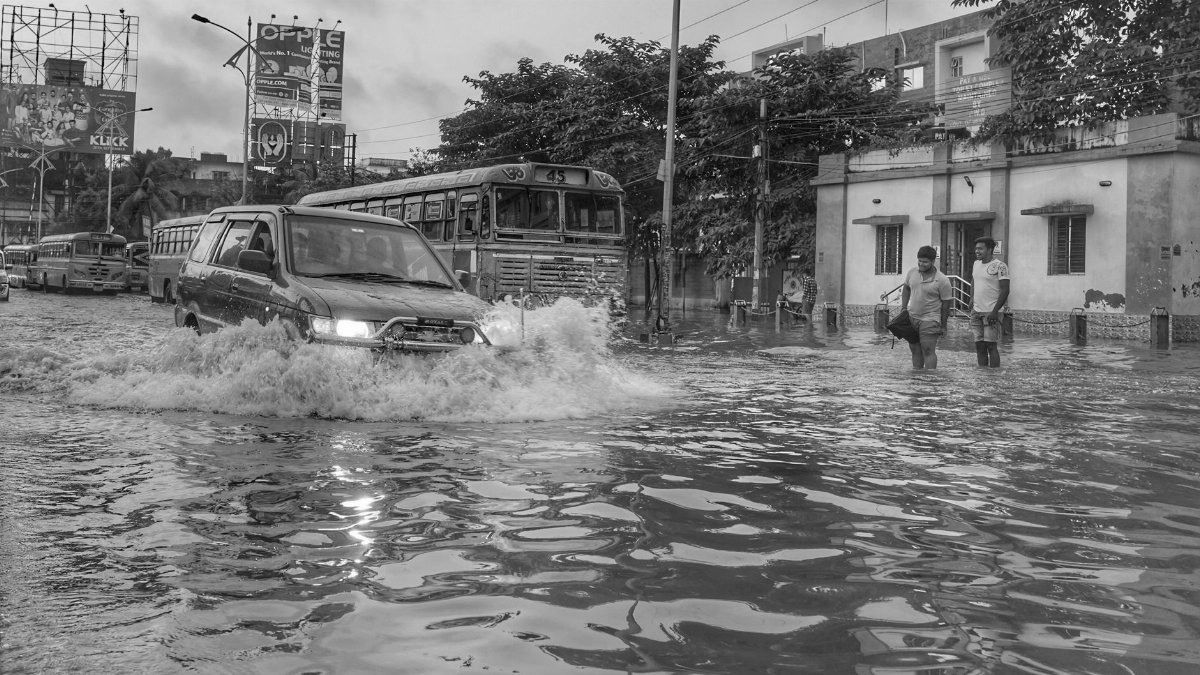 Flooded street scene in Kolkata, India, showcasing vehicles and people affected by monsoon rains.