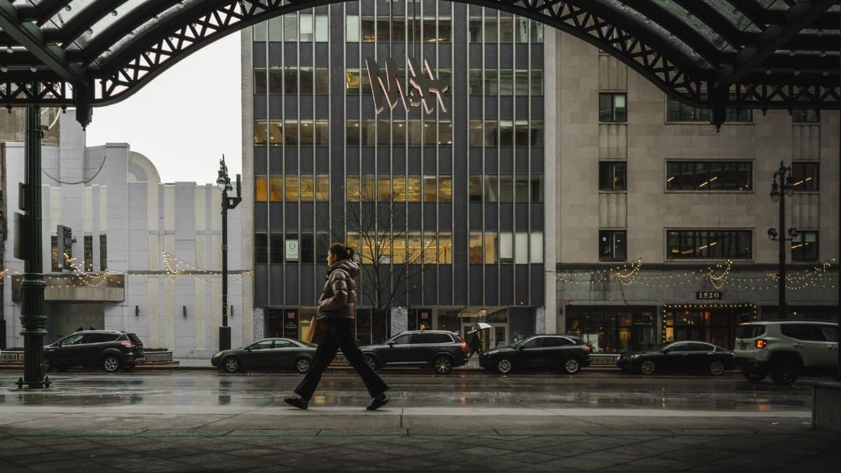 A person walks in downtown Detroit, MI, showcasing urban life amidst rain and city lights.