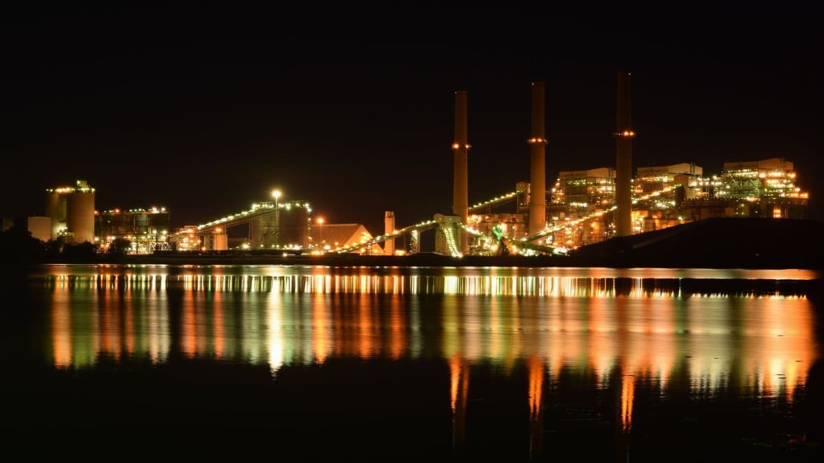 A brightly lit industrial plant reflected in a river at night creates a dramatic scene.