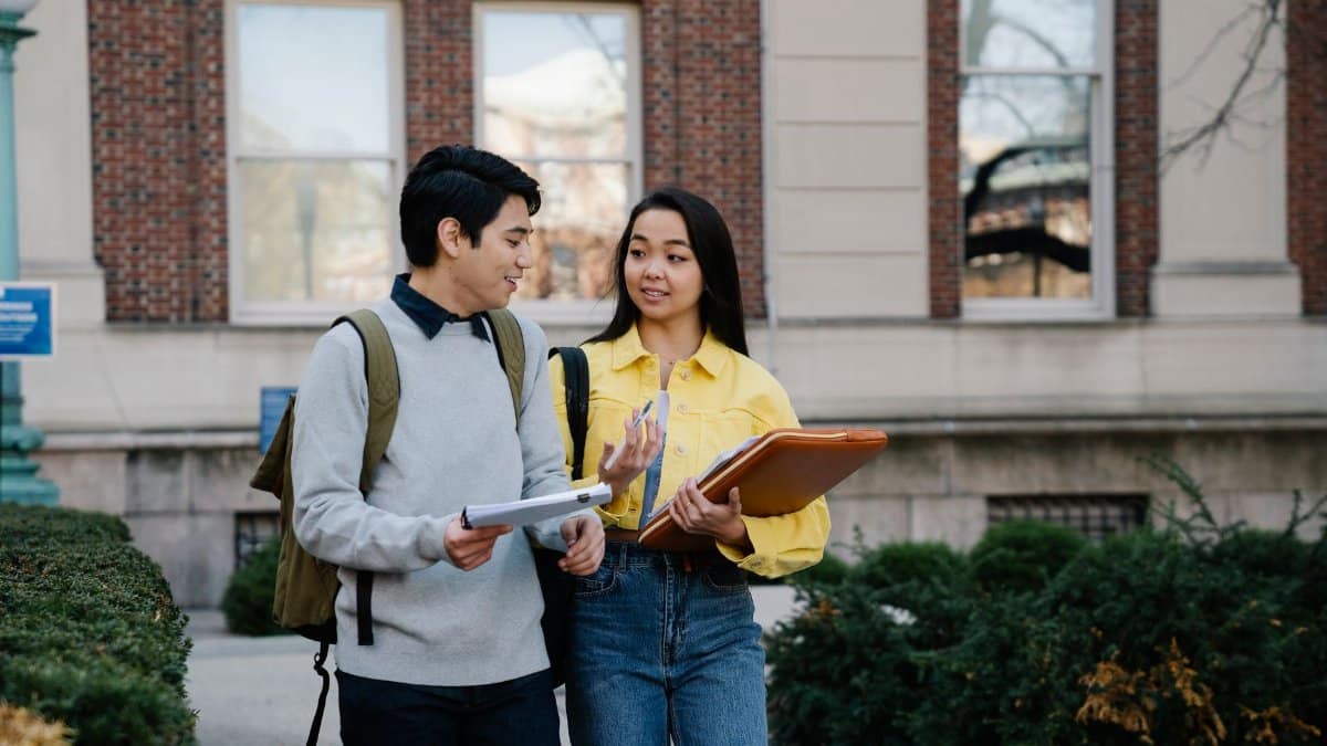 Two college students walking and discussing on campus with books.