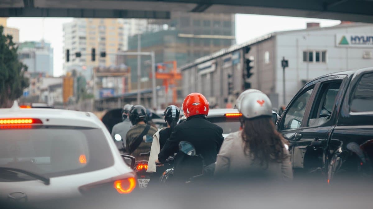 City street view filled with cars and motorcyclists waiting at traffic lights.