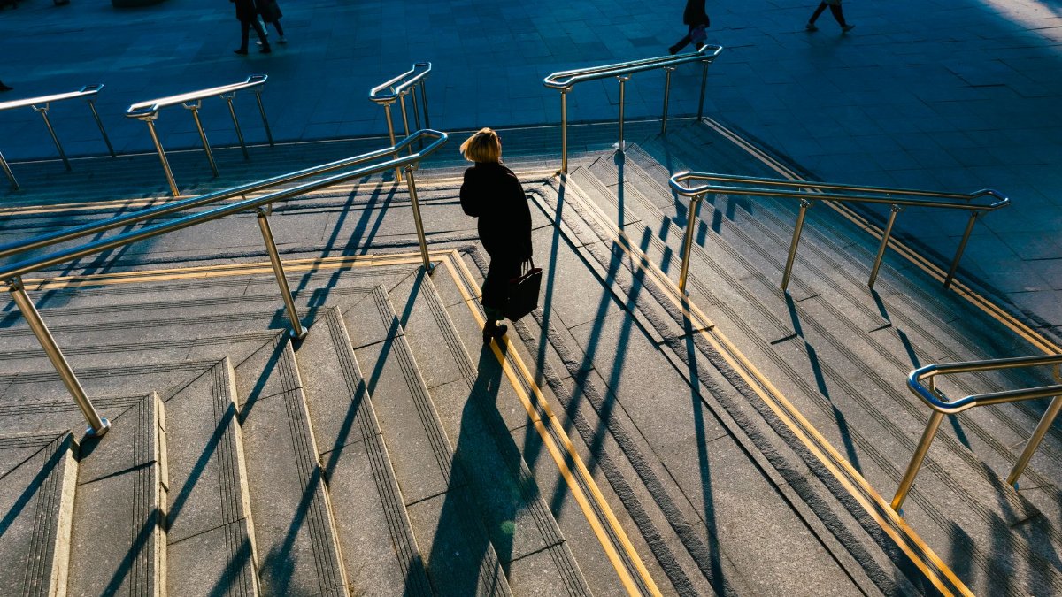 A person walking down a sunlit city staircase casting long shadows, illustrating urban life.