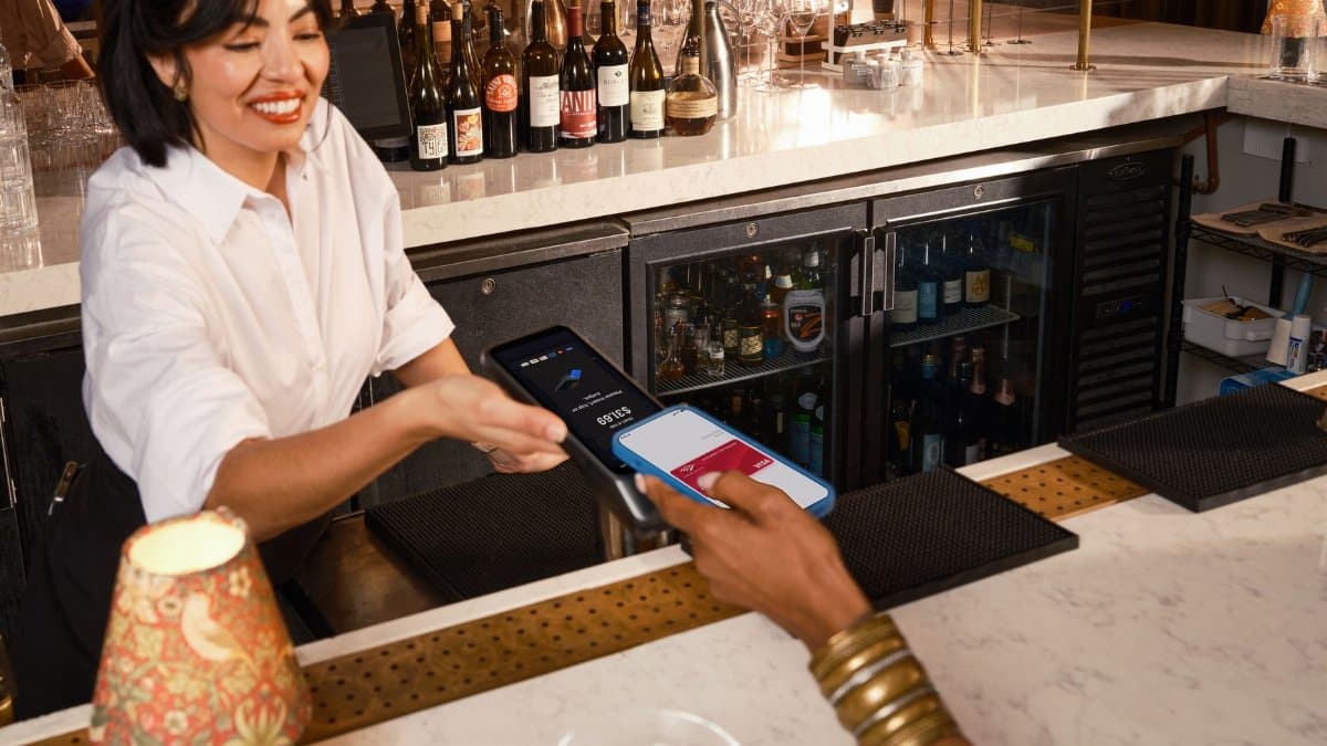 A bartender assists a customer with contactless mobile payment at an upscale bar.