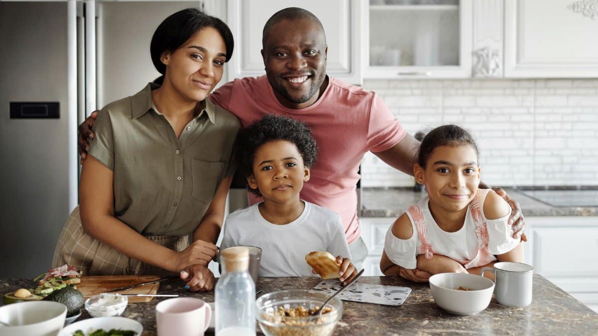 A joyful family of four smiling together at the kitchen counter during breakfast time.