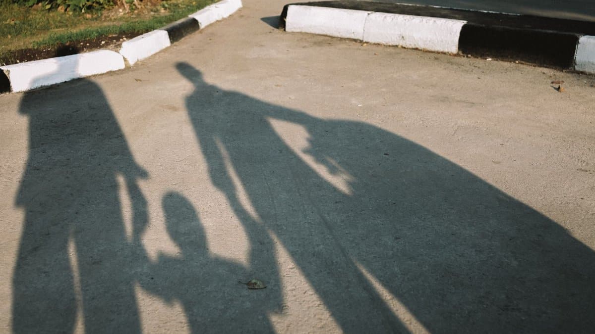 Silhouettes of a family holding hands cast shadows on a sunny pavement.
