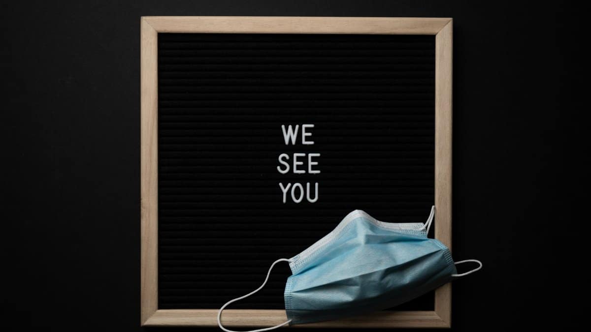 From above blackboard in wooden frame with white text on center under medical mask against black background