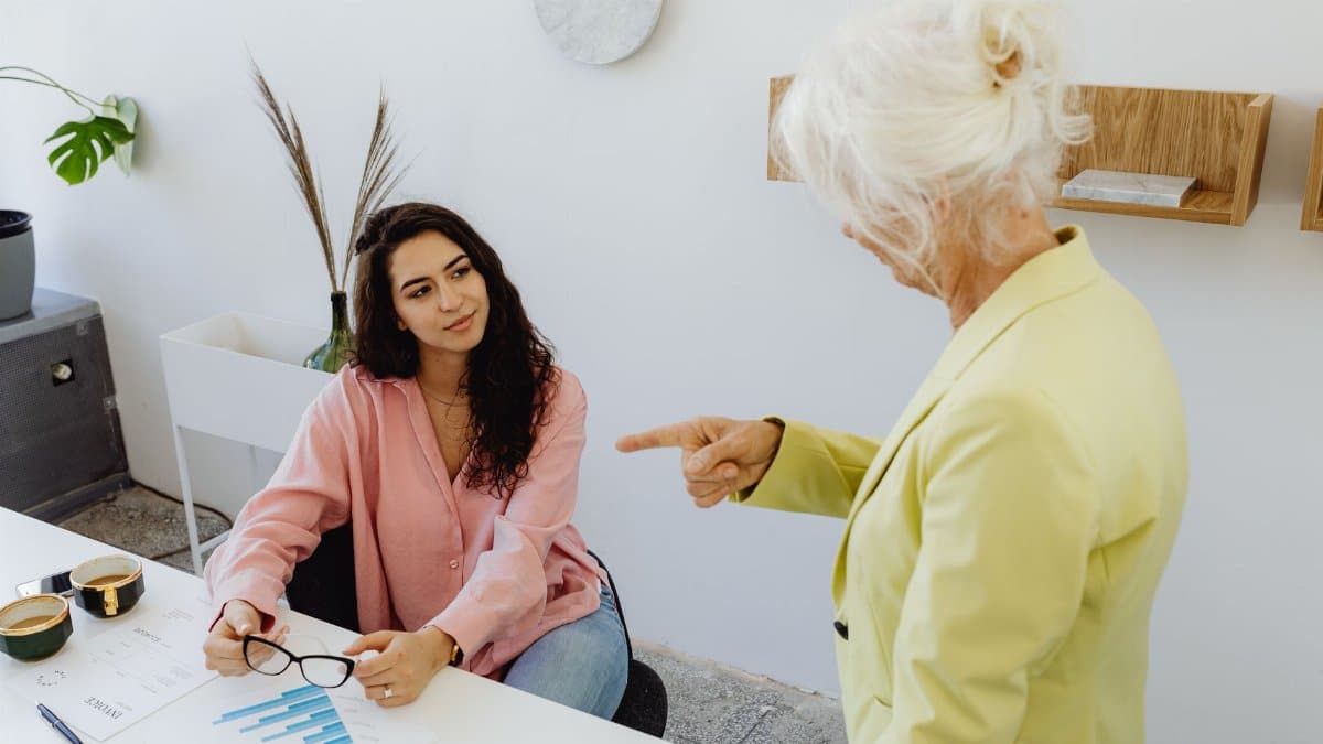 A senior woman in leadership discussing with a young businesswoman at a modern office desk.