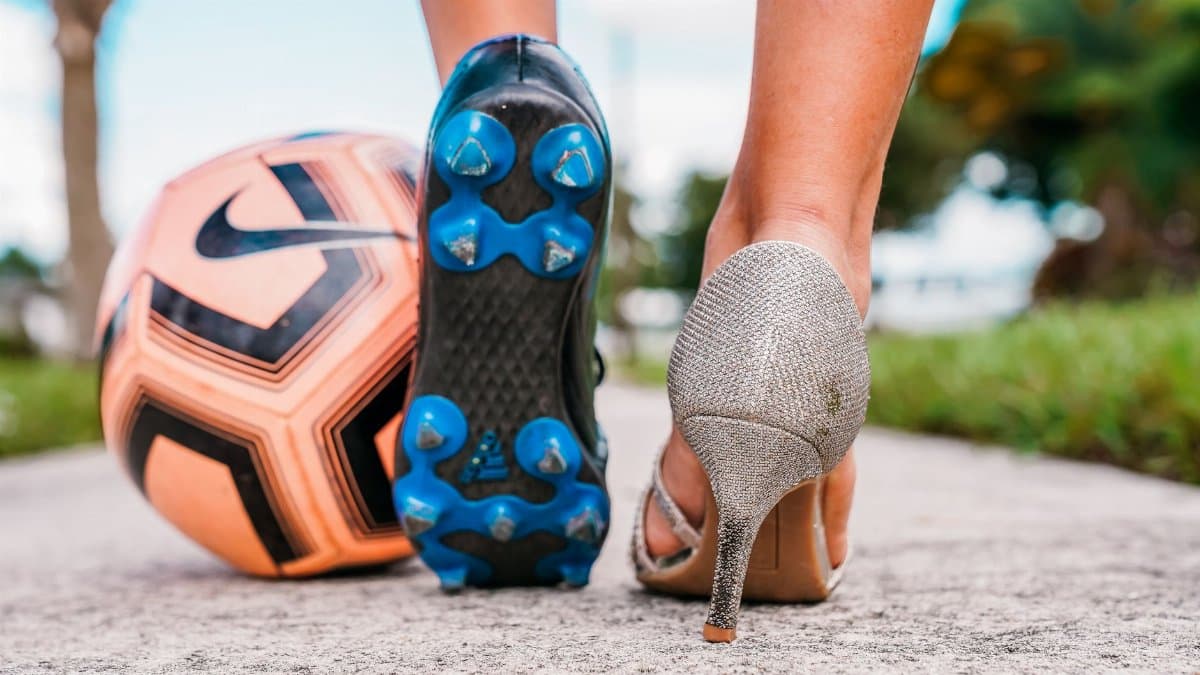 Juxtaposition of a soccer cleat and high heel on a sunny path, symbolizing diversity.
