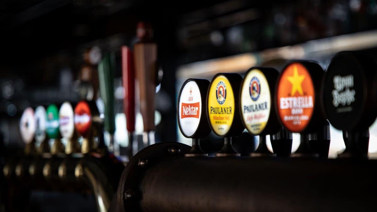 Close-up of assorted beer taps in a dimly lit bar, showcasing various brewery logos and selections.