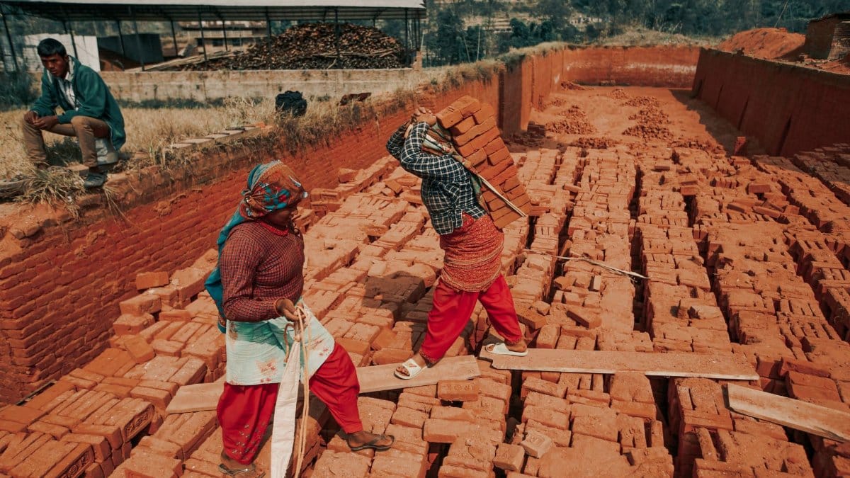 Two workers carrying bricks at an outdoor construction site, showcasing teamwork and labor.