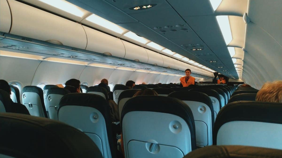 Inside of modern airplane cabin with passengers sitting on comfortable seats and cabin crew standing at passageway