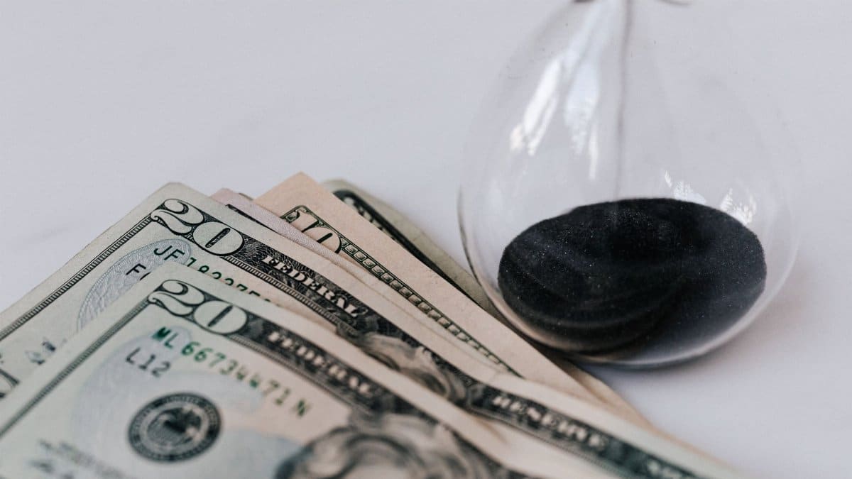 From above transparent hourglass with flares on fragile surface near pile of banknotes with numbers and official seal