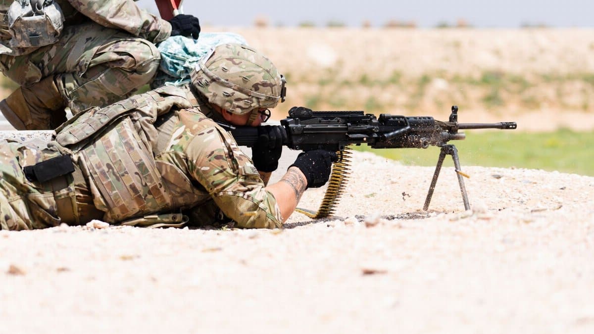 US soldier in camouflage uniform using a machine gun in outdoor military training.