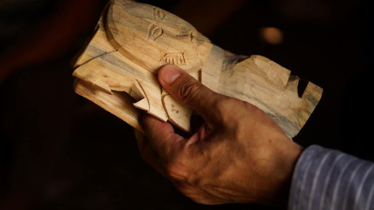 Artisan holding a handcrafted wooden mask in Yaxcabá, Mexico. Close-up shows detailed carving.