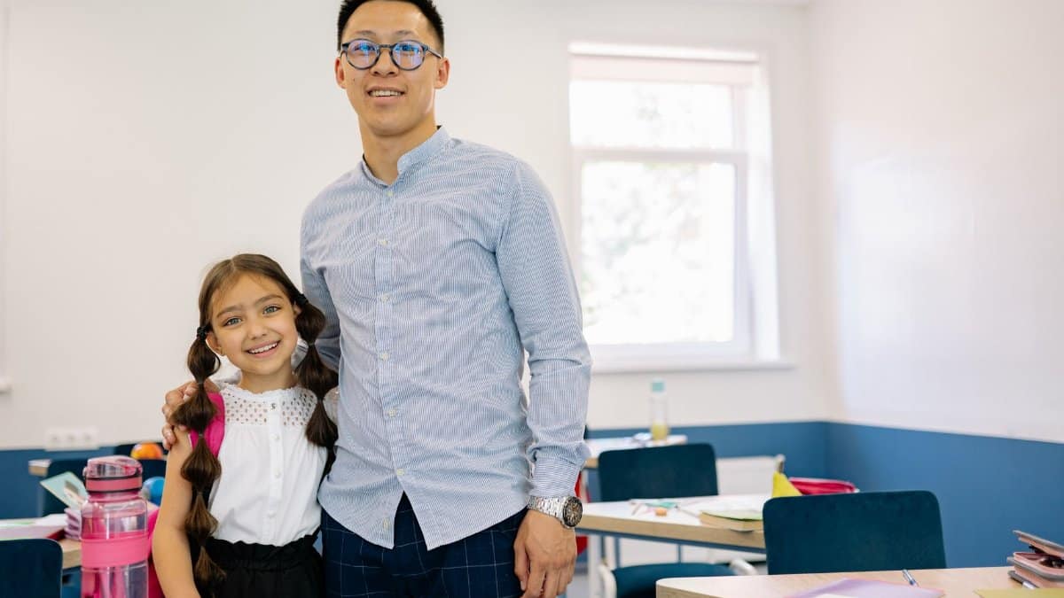 Male teacher and female student smiling together inside a classroom setting.