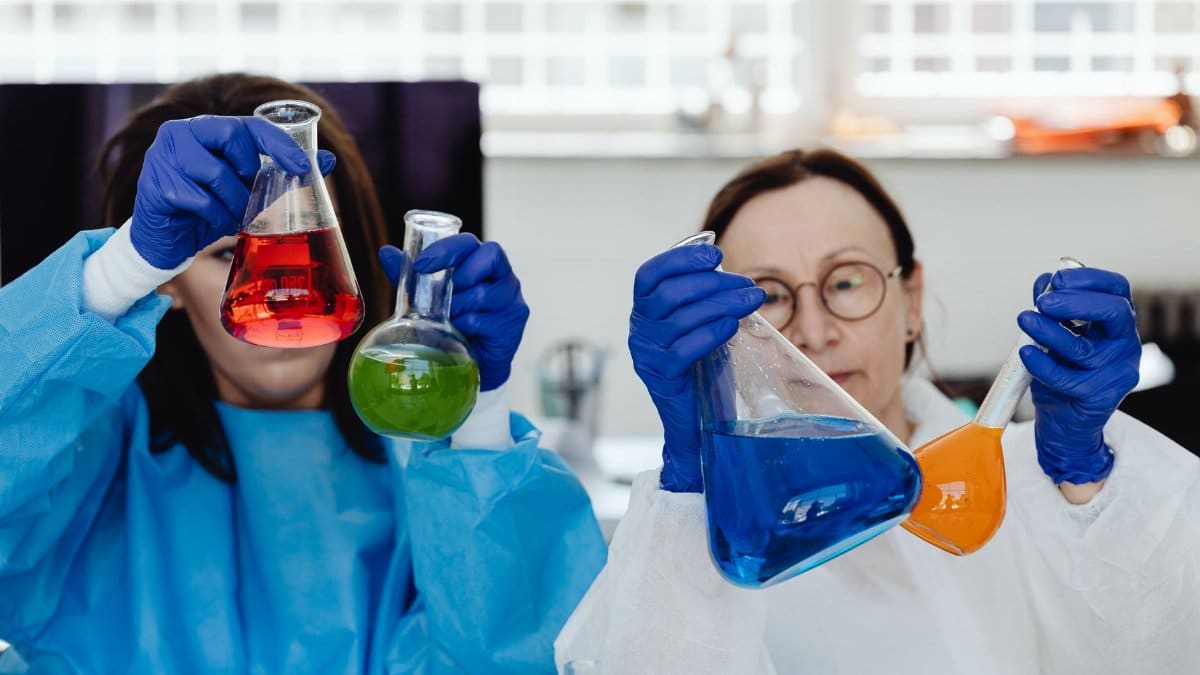 Two female scientists perform experiments with colorful chemicals in a lab environment.