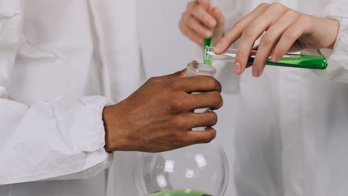 Close-up of researchers pouring green liquid between test tubes in a laboratory.