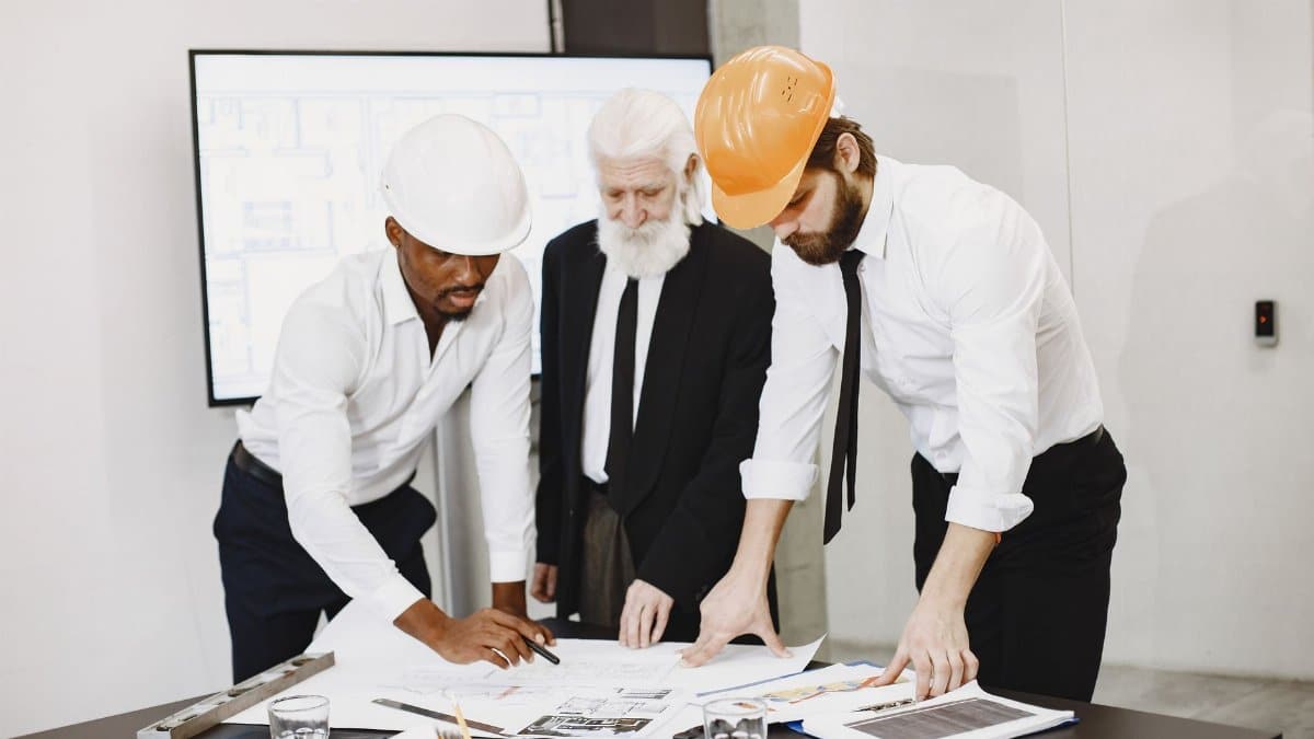 Three professionals in an office setting reviewing building plans and collaborating on a construction project.