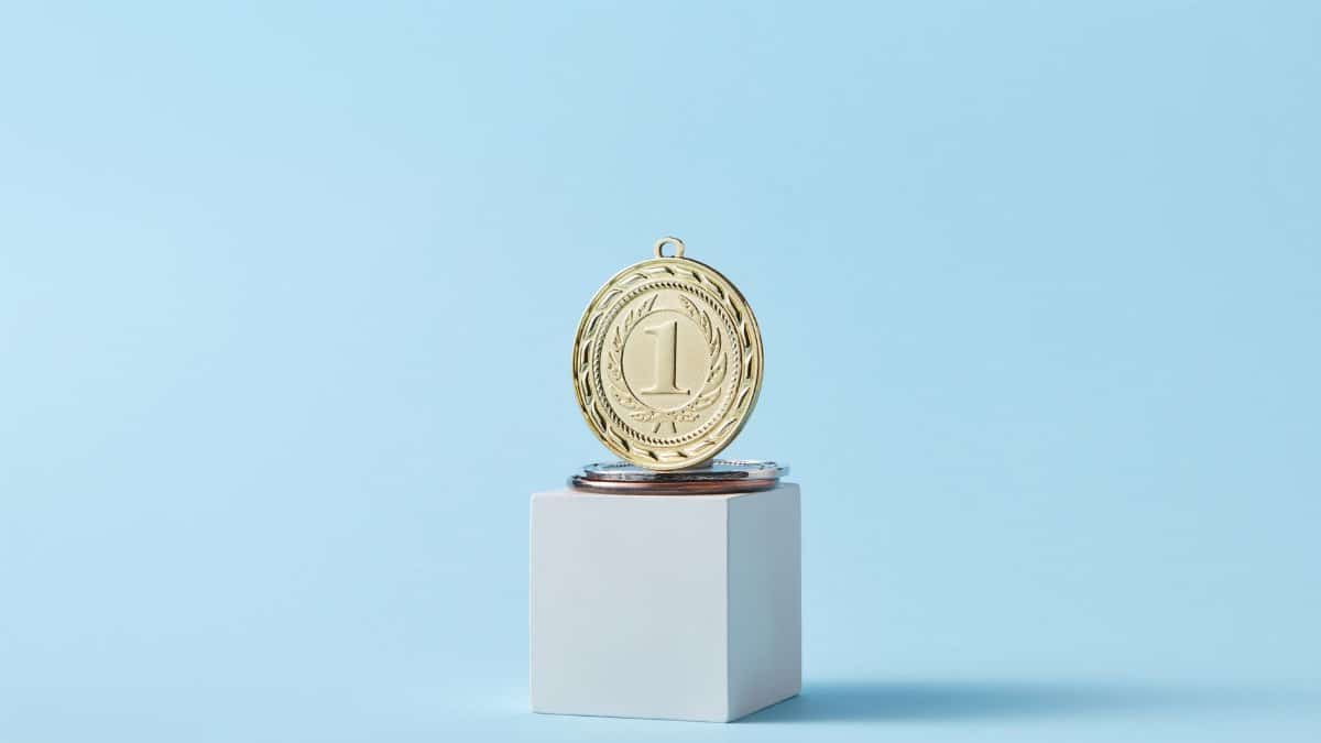 Close-up of a gold medal on a podium with a baby blue background, symbolizing victory.