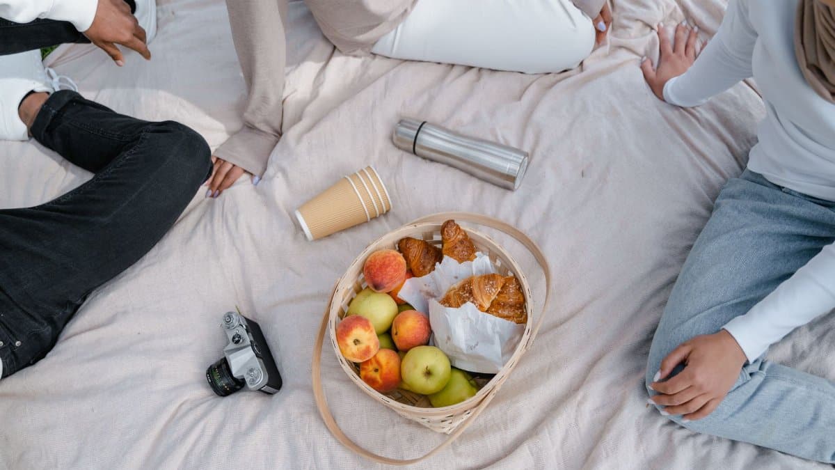 Relaxing outdoor picnic scene with fruits, pastries, and friends enjoying a sunny day.