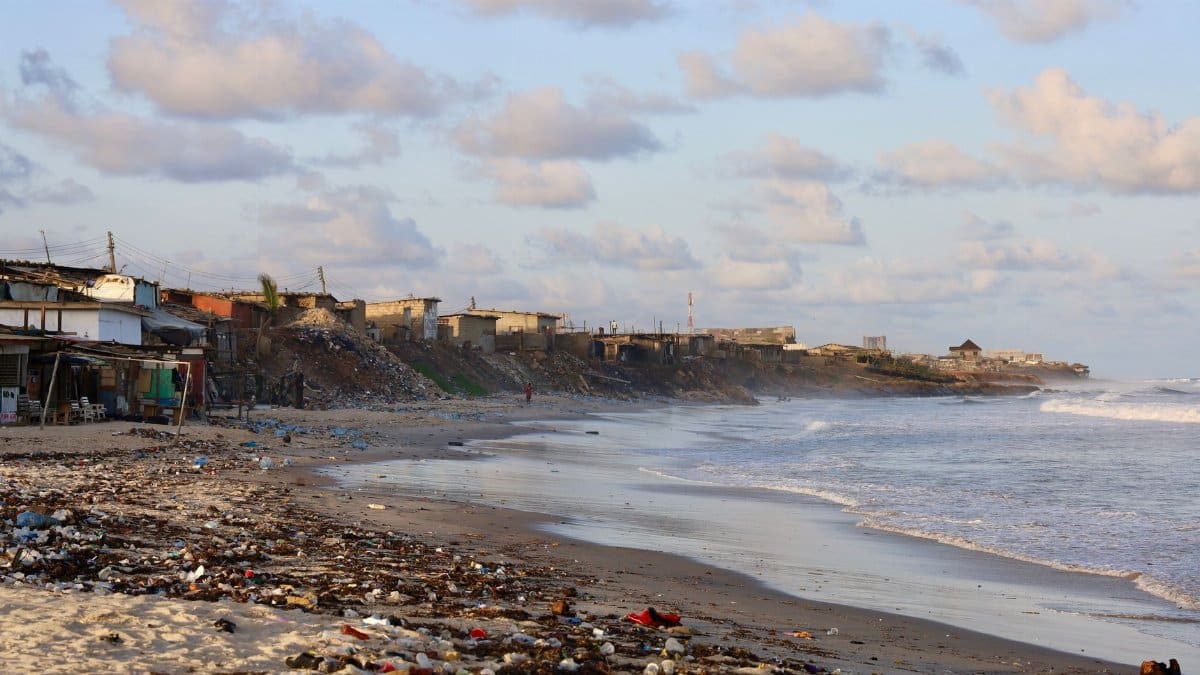 Coastal pollution littering a beach in Accra, Ghana, with buildings in the background.