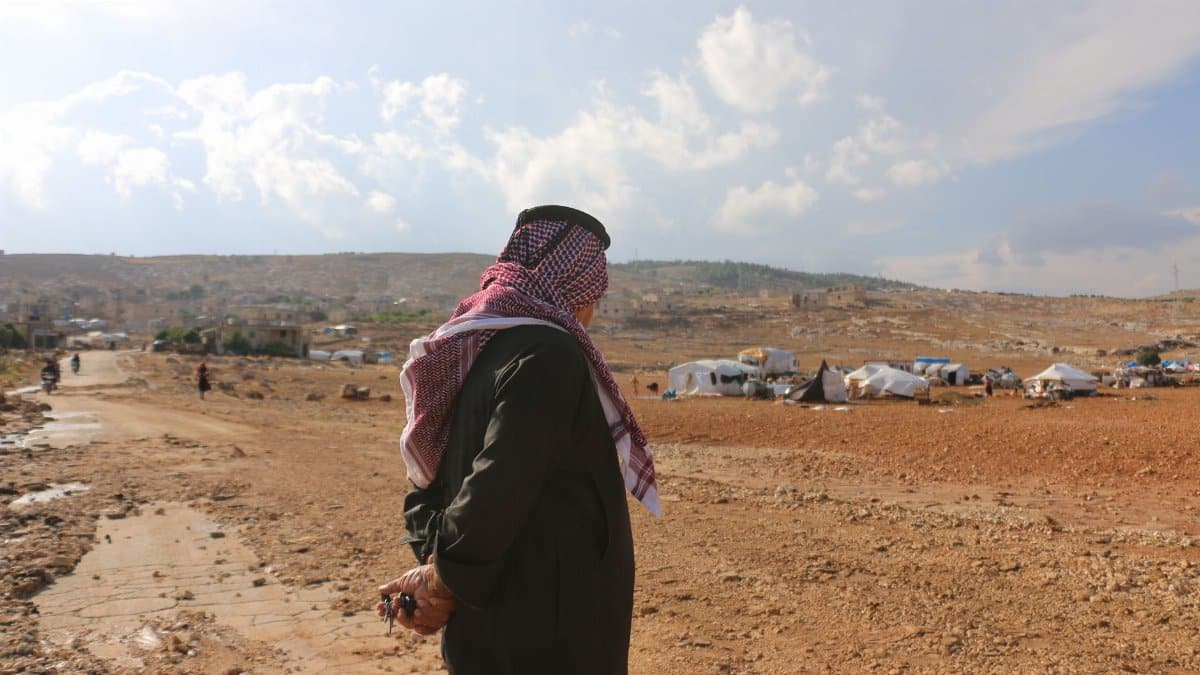 Side view of anonymous male wearing traditional Muslim dishdasha standing in valley with tents for homeless