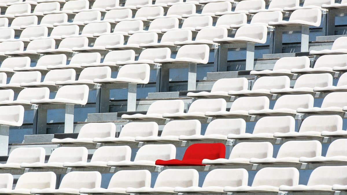 A striking red chair stands out in a sea of white stadium seats, symbolizing individuality.