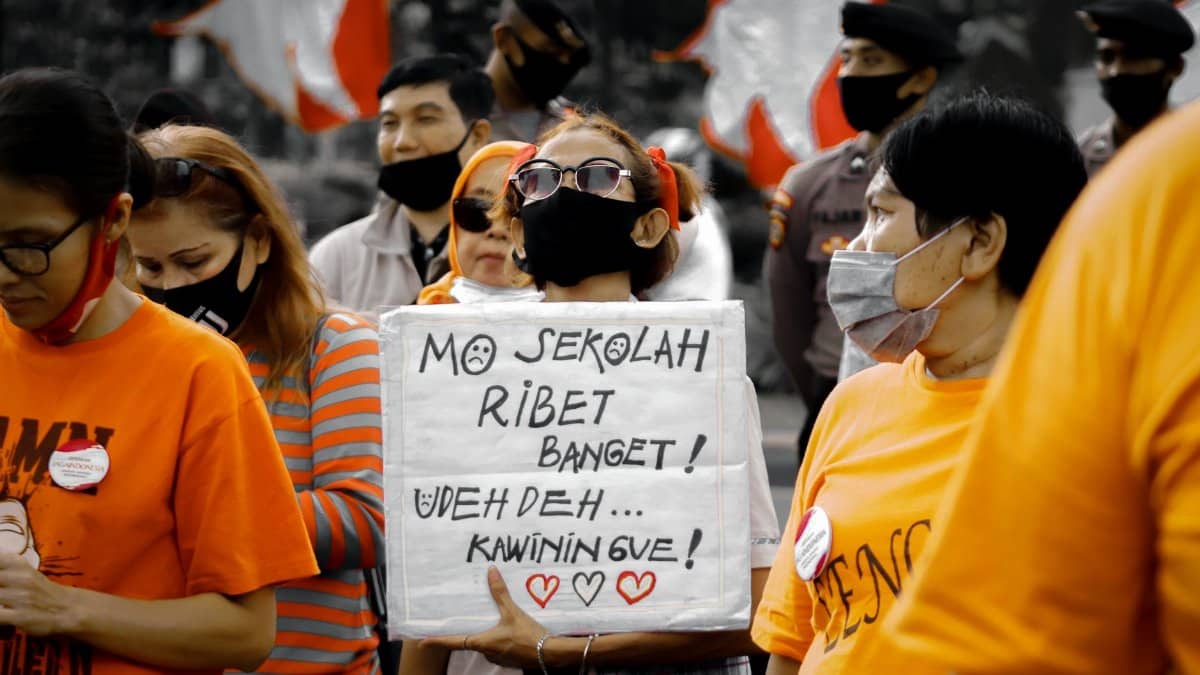 Protesters in Jakarta hold signs expressing social issues, amid a crowd wearing face masks.