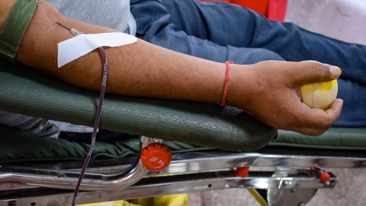 Detail view of a man's arm donating blood in a hospital environment, emphasizing healthcare support.