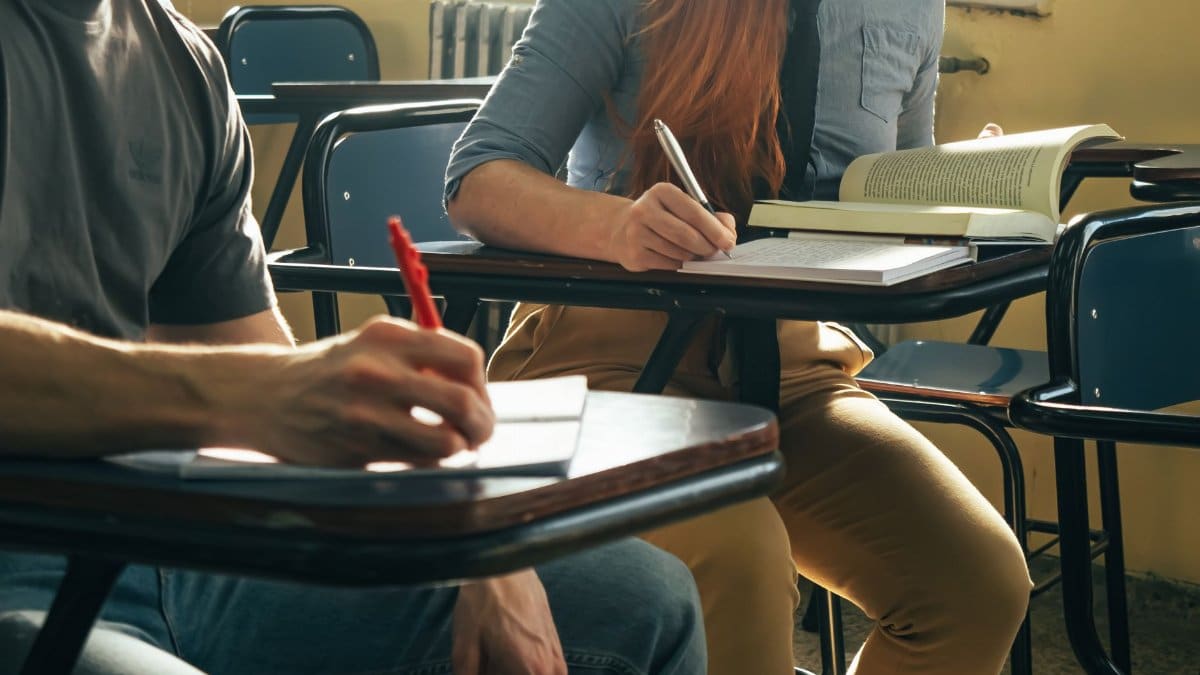 Two students writing notes in a classroom setting, focusing on study and education