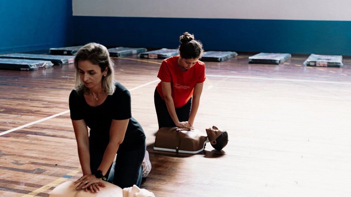 Two women learn CPR techniques on mannequins during a first aid training session.