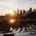 A tractor at a construction site with city skyline and sunset background, reflecting urban development.