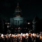 A large crowd protesting for civil rights at night in front of the Denver Capitol building.