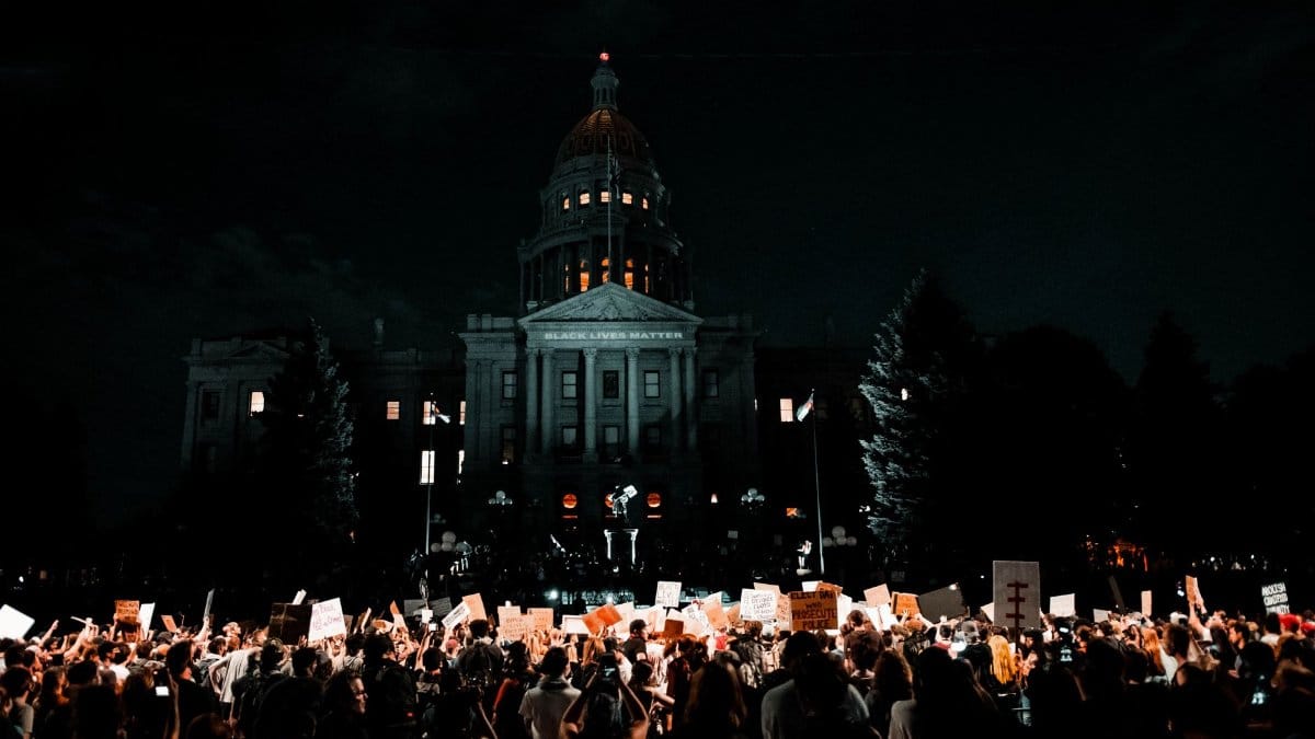 A large crowd protesting for civil rights at night in front of the Denver Capitol building.