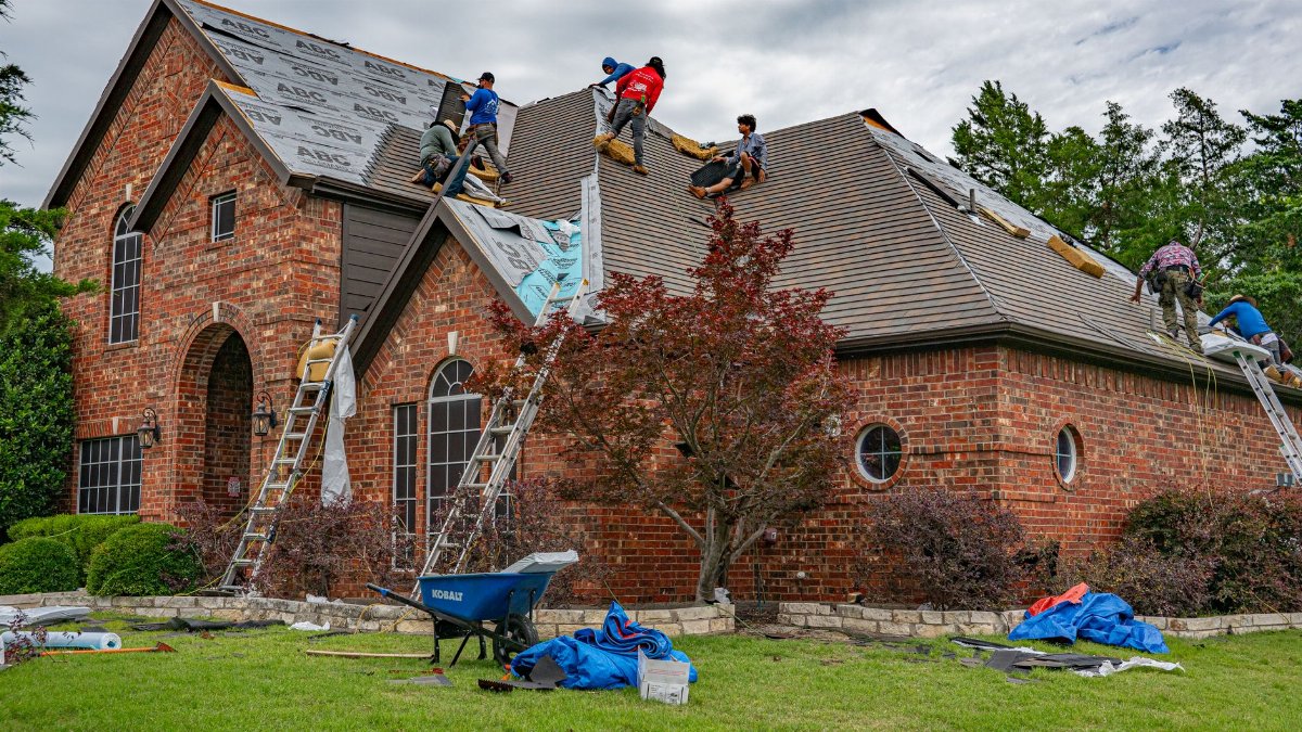 Roofers working on brick home in Allen, Texas, addressing shingles and roofing materials.
