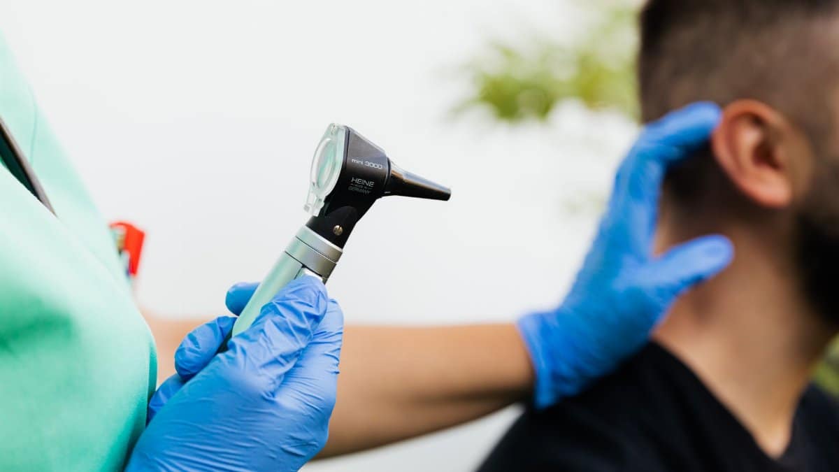 Healthcare professional examining patient's ear with an otoscope in a clinical setting.