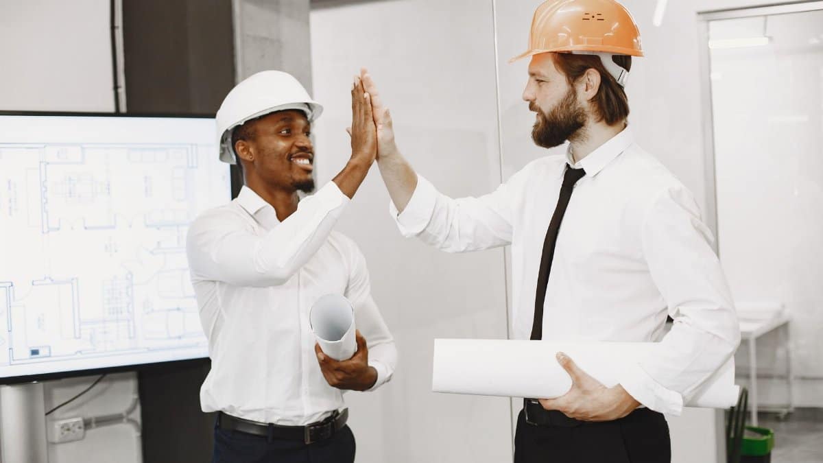 Two engineers in safety helmets celebrate a successful plan with a high-five indoors.