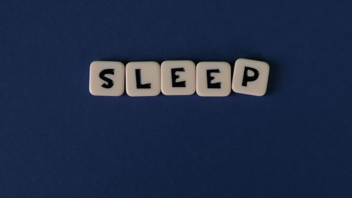 White letter tiles spelling 'SLEEP' against a dark navy background, highlighting simplicity and rest.