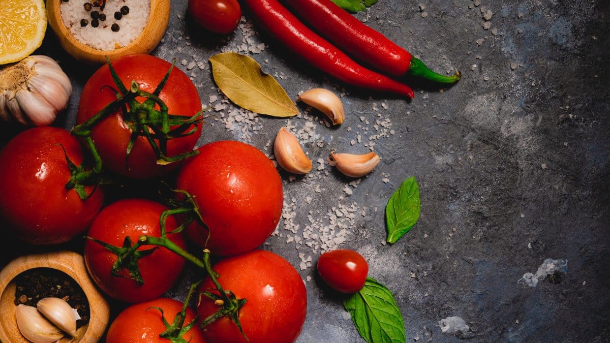 A vibrant collection of fresh tomatoes, chili peppers, and herbs on a rustic surface.