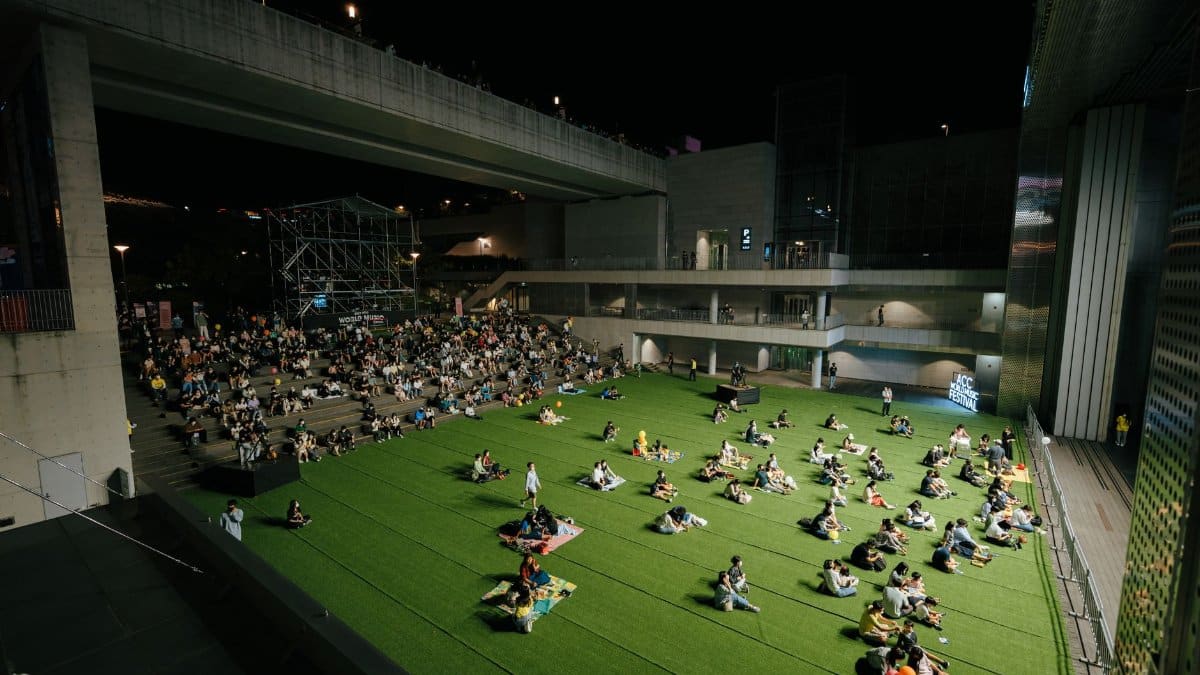 A vibrant night event with people gathered on artificial grass under a modern structure.