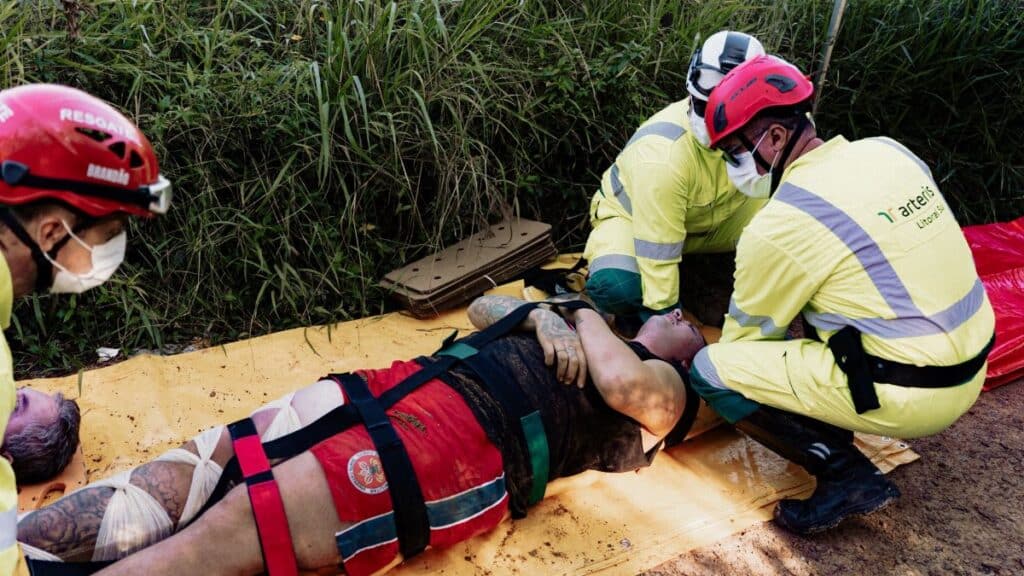 Rescue operation with paramedics attending to an injured person outdoors. Wearing protective helmets and face masks.