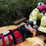 Rescue operation with paramedics attending to an injured person outdoors. Wearing protective helmets and face masks.