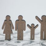 Wooden family figurines on dollar bills symbolizing financial stability.