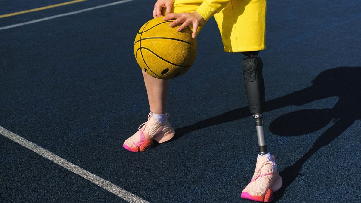 Close-up of an adaptive athlete with a prosthetic leg holding a basketball on a sports court.