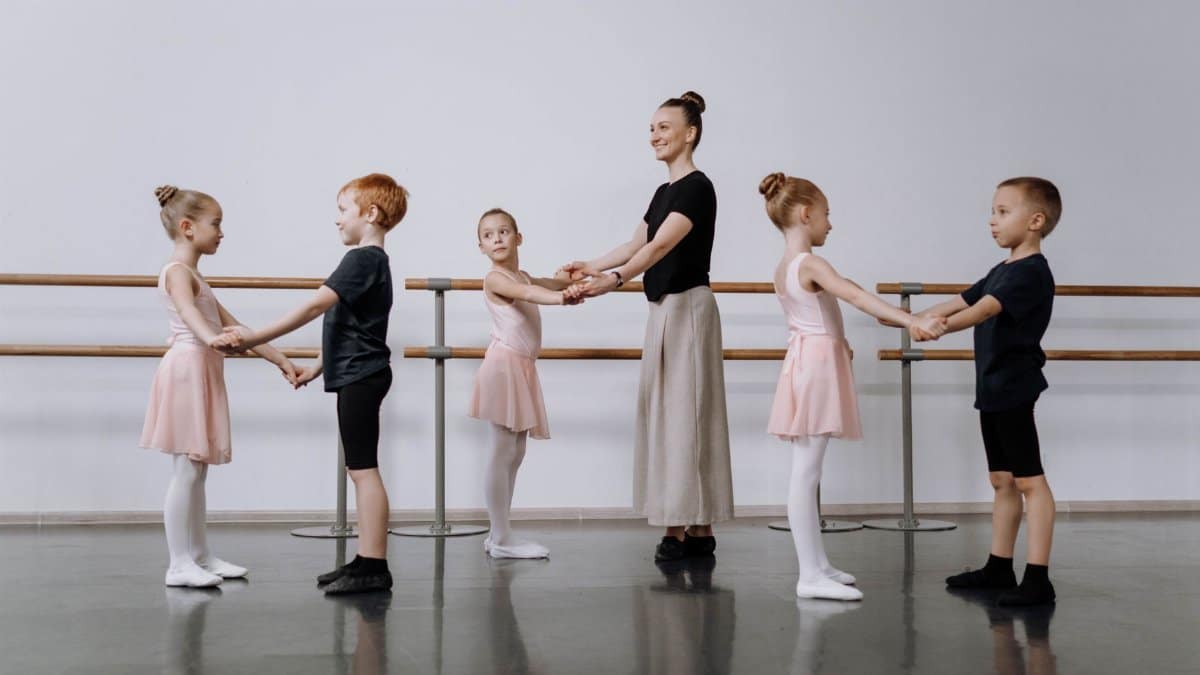 Instructor guides children in ballet class, focusing on dance basics.
