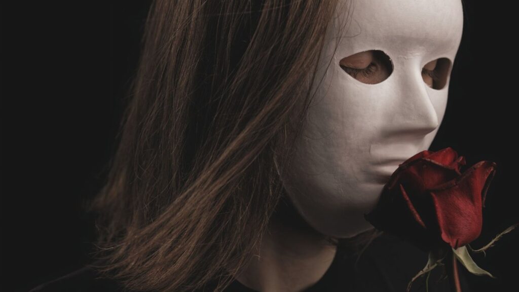 Mysterious portrait of a person with a white mask holding a red rose. Dark and intriguing mood.