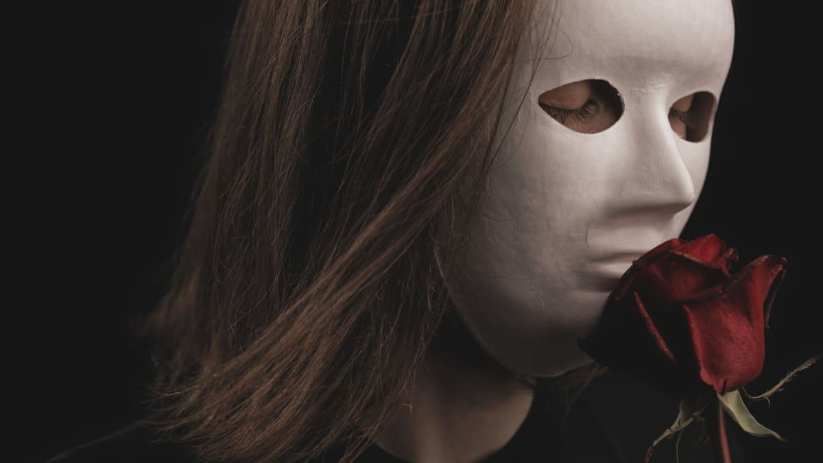 Mysterious portrait of a person with a white mask holding a red rose. Dark and intriguing mood.