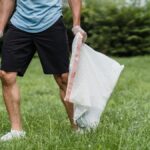 A volunteer cleaning a park, holding a grabber and garbage bag, promoting environmental well-being.