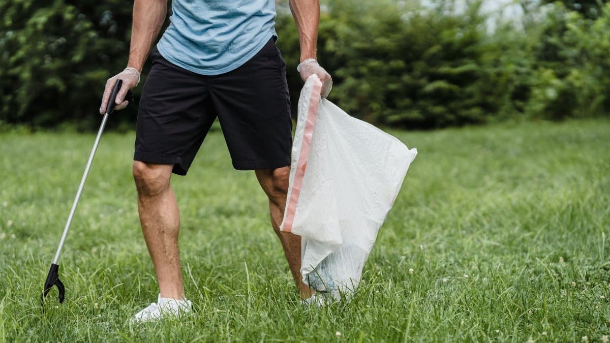 A volunteer cleaning a park, holding a grabber and garbage bag, promoting environmental well-being.