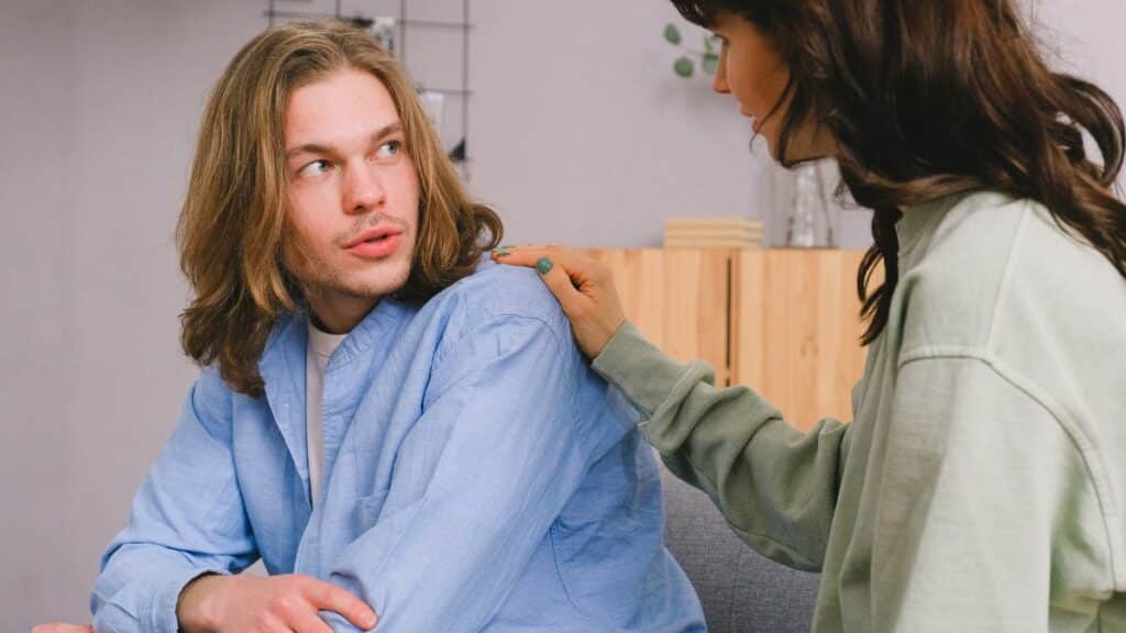 Concentrated woman talking and touching shoulder of pensive male in light room in daytime